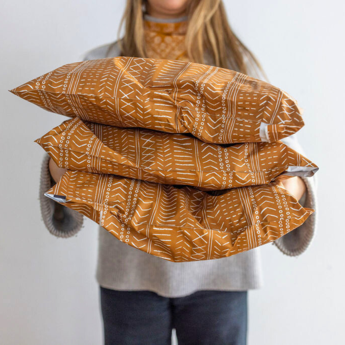 Woman holding Favorite Supplies' Boho Brown Poly Mailer in hand for a size comparison. Illustrates the stylish design and compact size (10x13) for convenient use.