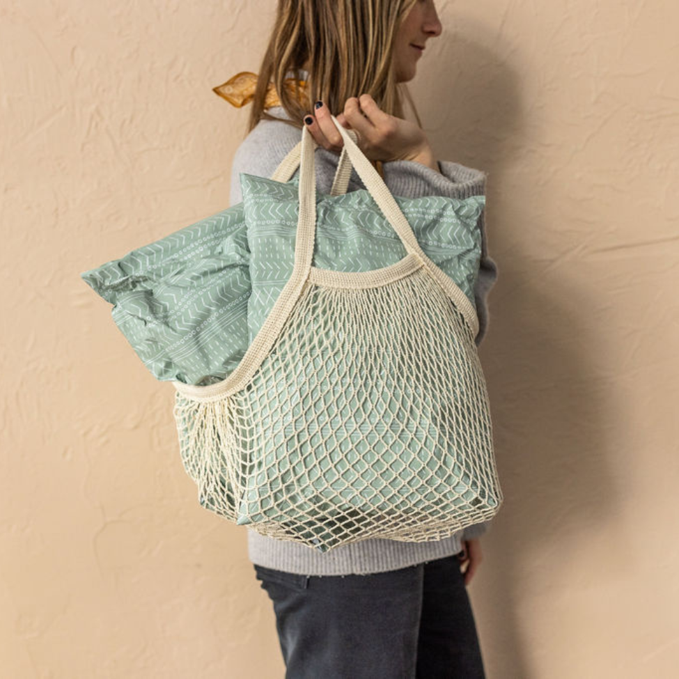 Woman against a wall, holding a Bohemian see-through bag with 10x13 Green Geo Boho Poly Mailers inside. Stylish packaging for small business shipping.