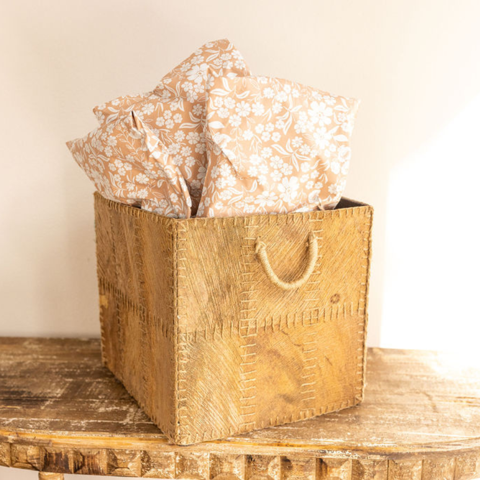 Bohemian basket filled with 10x13 Floral Dusty Pink Poly Mailers, standing on a table against the wall with sunlight streaming in. A stylish and functional display for efficient shipping by Favorite Supplies.