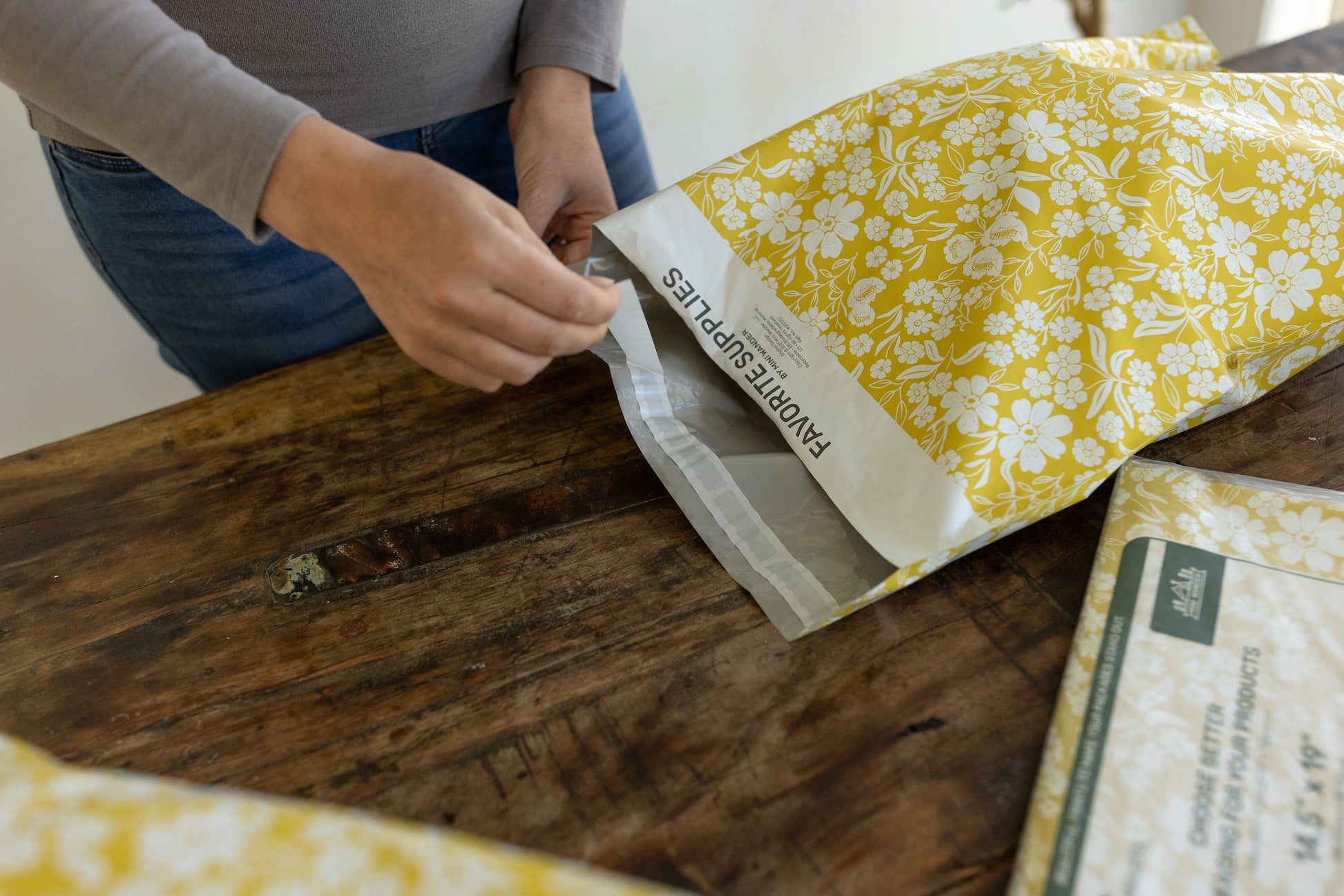 The process of fulfilling orders. A small business owner is using a quick peel and seal adhesive to package a parcel. Using fun yellow flowery polymailer bags.