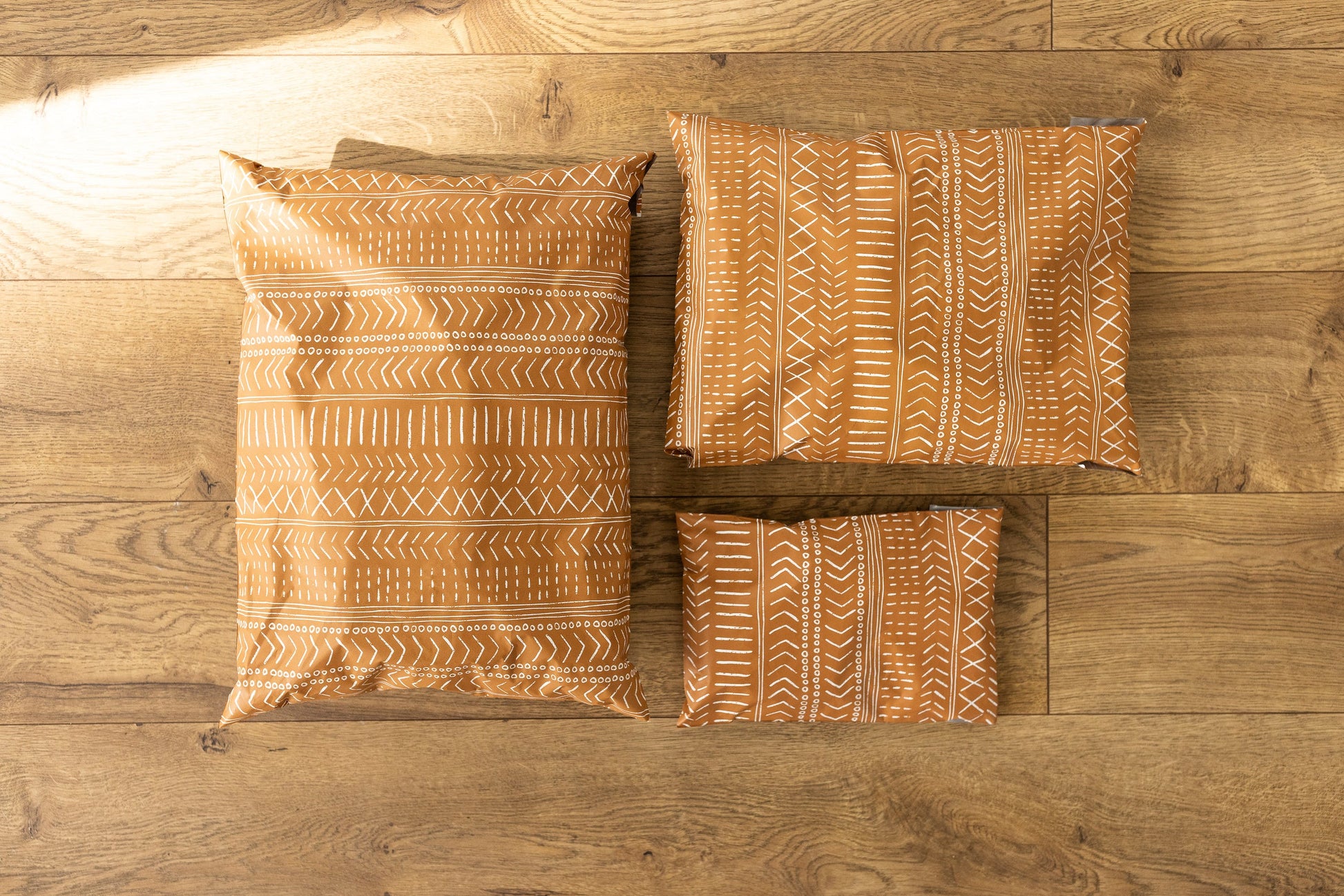 A photo comparing different sized poly mailers. Brown color with white block printed boho line design. Pictured are sizes 12x15.5 , 10x13 and 6x9 self sealing plastic shipping envelopes.